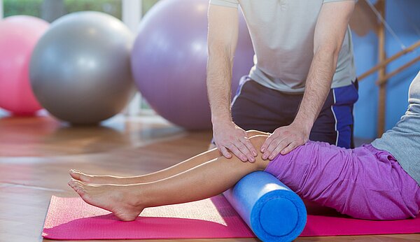 Physiotherapeut macht Übungen mit einer Patientin auf Schaumrolle