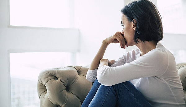 Eine Frau sitzt auf einem Sofa und schaut aus dem Fenster