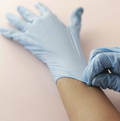 Eine Hand zieht einen blauen Einweghandschuh über eine andere Hand