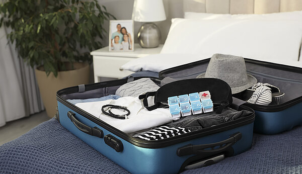 Auf einem Bett liegt ein offener Koffer mit Medikamenten darin