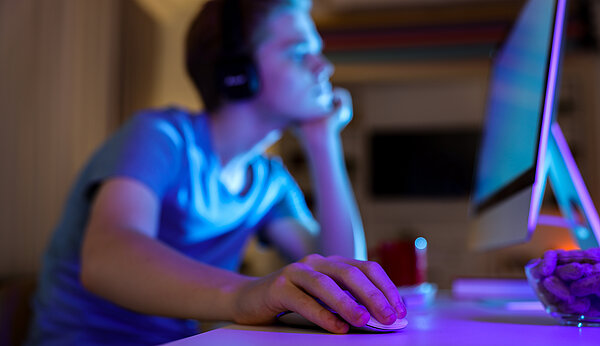 Jugendlicher sitzt allein in dunklem Zimmer vor einem PC