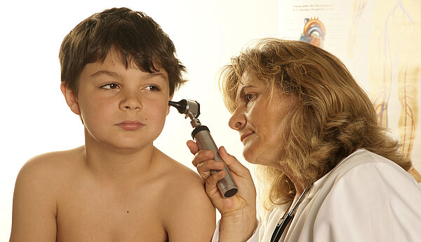 Eine Frau untersucht das Ohr eines Kindes