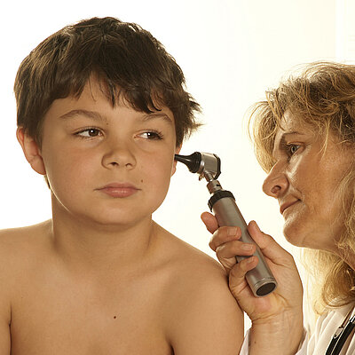 Eine Frau untersucht das Ohr eines Kindes