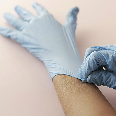 Eine Hand zieht der anderen einen Einweghandschuh über