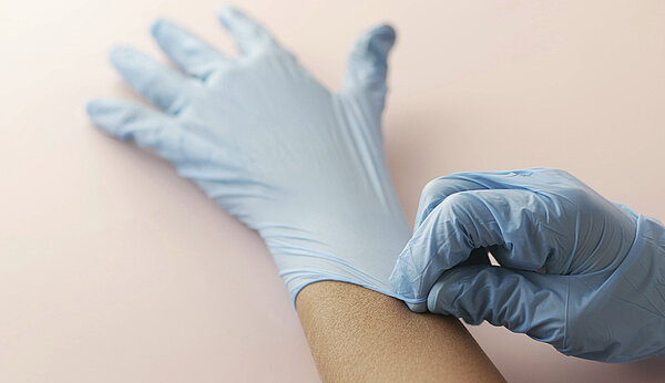 Eine Hand zieht der anderen einen Einweghandschuh über