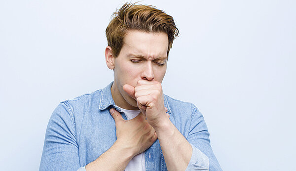 Ein Mann hustet und hält sich dabei den Brustkorb