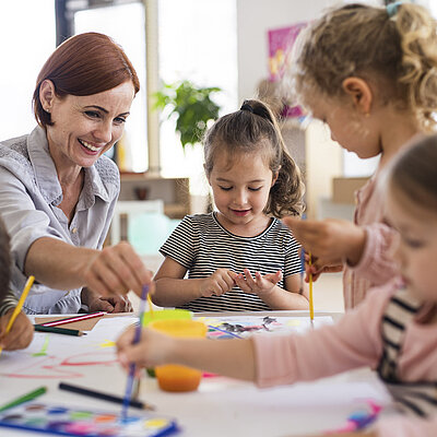 Eine Frau bastelt mit vier Kindern an einem Tisch
