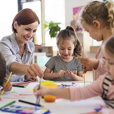 Eine Frau bastelt mit vier Kindern an einem Tisch