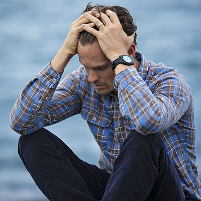 Ein Mann stützt den Kopf in beide Hände und schaut vor sich hin