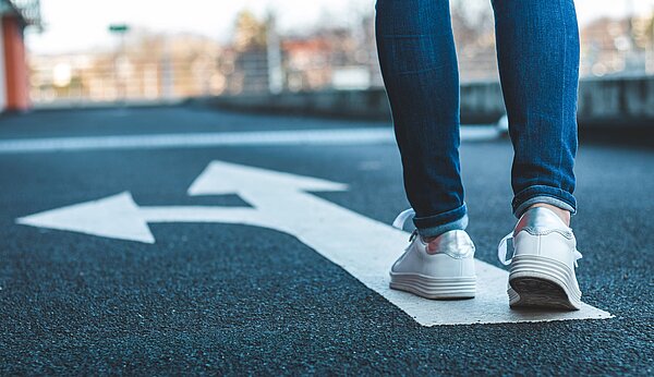 Symbolbild eine Person steht auf einer Straße auf einem gemalten Abbiegepfeil.
