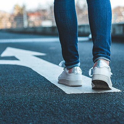 Symbolbild eine Person steht auf einer Straße auf einem gemalten Abbiegepfeil.