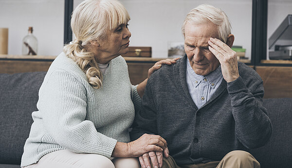 Eine weibliche Seniorin sitzt neben einem männlichen Senior und hat ihm die Hand auf die Schulter gelegt